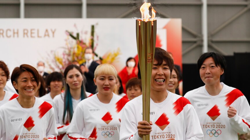 A Japanese woman in a red and white soccer uniform holding a lit golden torch 