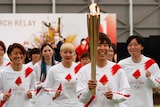 A Japanese woman in a red and white soccer uniform holding a lit golden torch 