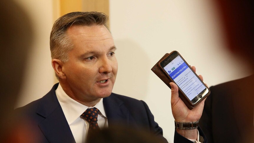 The words "election policies" under a Liberal Party banner appear on Chris Bowen's phone as he holds it up for the media to see