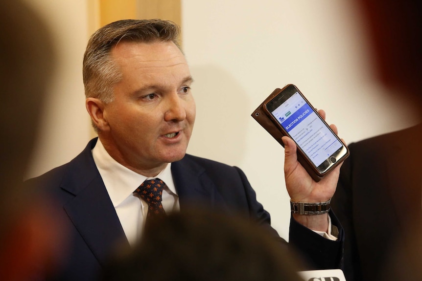 The words "election policies" under a Liberal Party banner appear on Chris Bowen's phone as he holds it up for the media to see