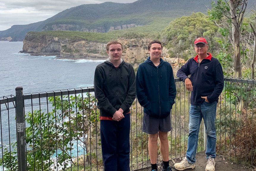 three men stand on a lookout in Tasmania with an ocean behind them 