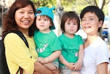 Two mothers pose with their twin girls, who are wearing matching outfits.