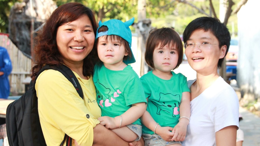 Two mothers pose with their twin girls, who are wearing matching outfits.