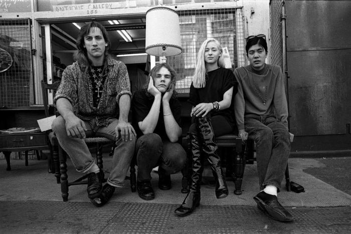 Four young people sit on antique chairs and stare at the camera.