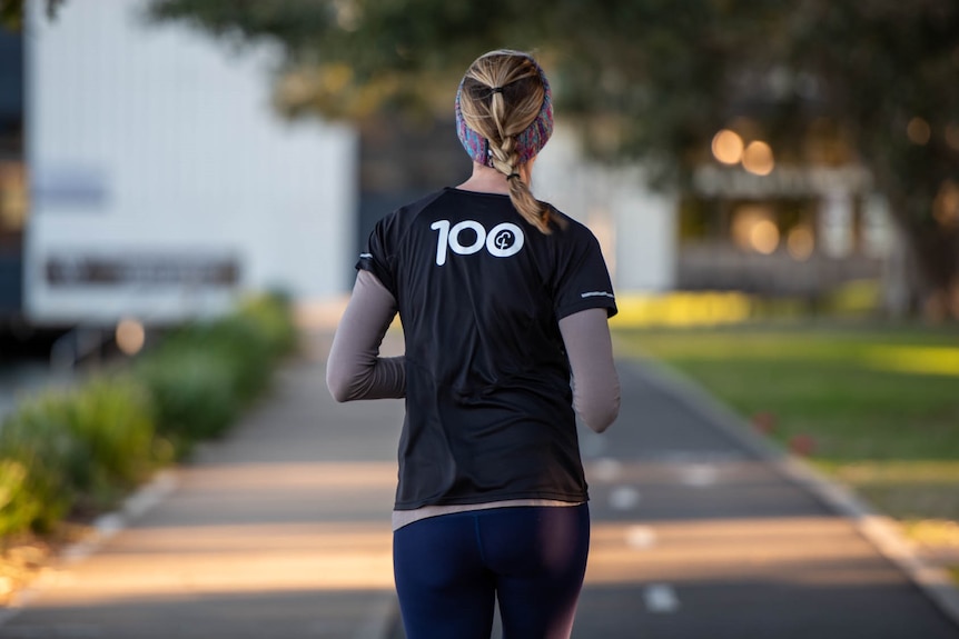 A photo of a woman from the back, running, with a black tshirt on with the number 100.