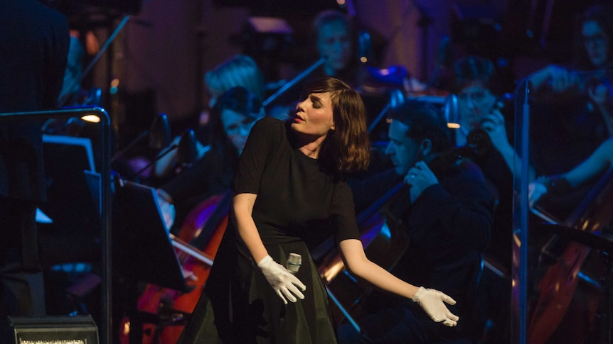 The singer Sarah Blasko swaying on stage with members of an orchestra in the background