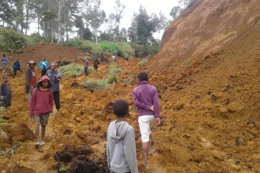 People walk through red dirt of a landslide.
