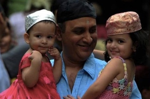 A Parsi man smiles as he holds his two children in his arms.
