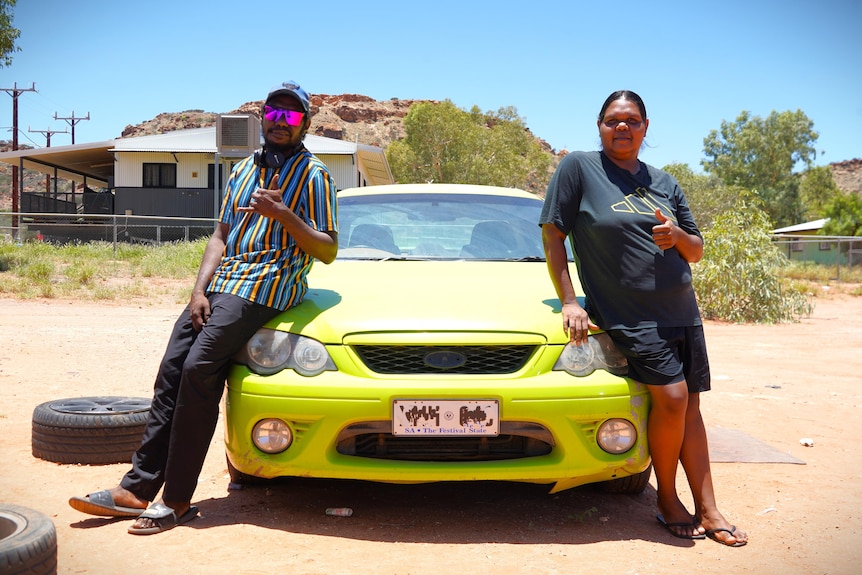 Two people in remote community lean on bonnet of lime green sedan