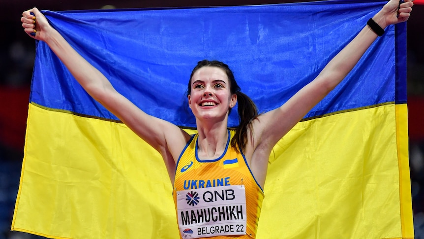 A women athlete holds up a blue and yellow flag