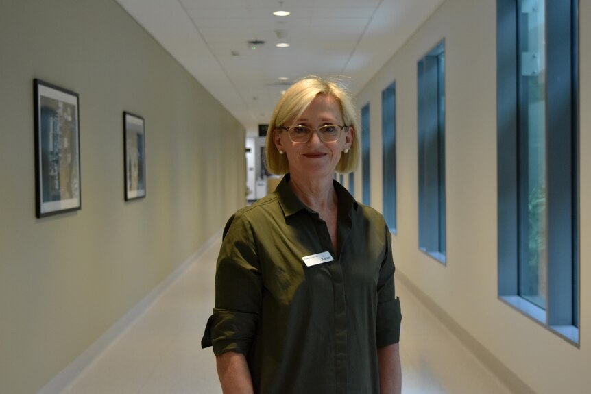 Woman in green shirt, glasses, standing in hospital hallway