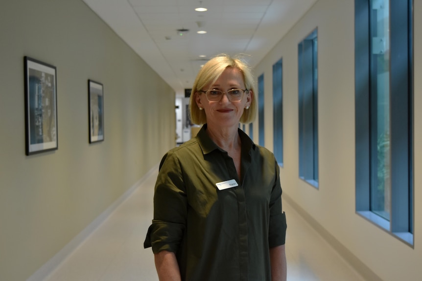 Woman in green shirt, glasses, standing in hospital hallway