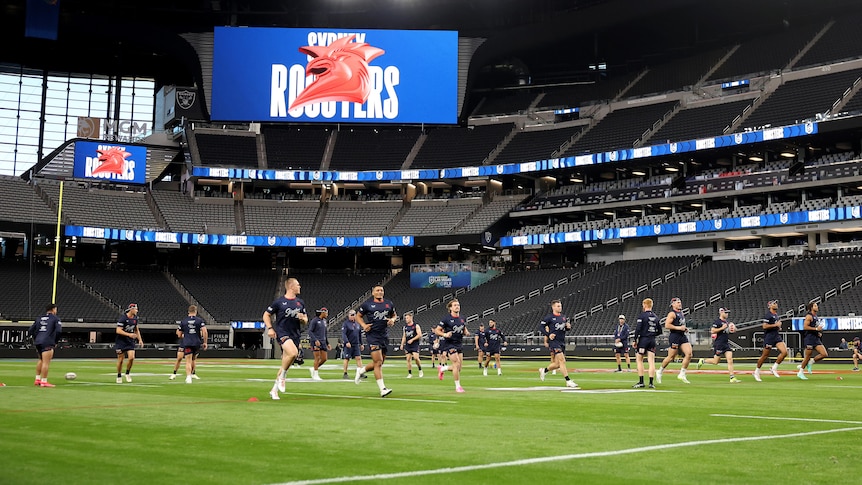 A group of NRL players have a team session running at an NFL stadium, with a sign on the big screen saying "Sydney Roosters".
