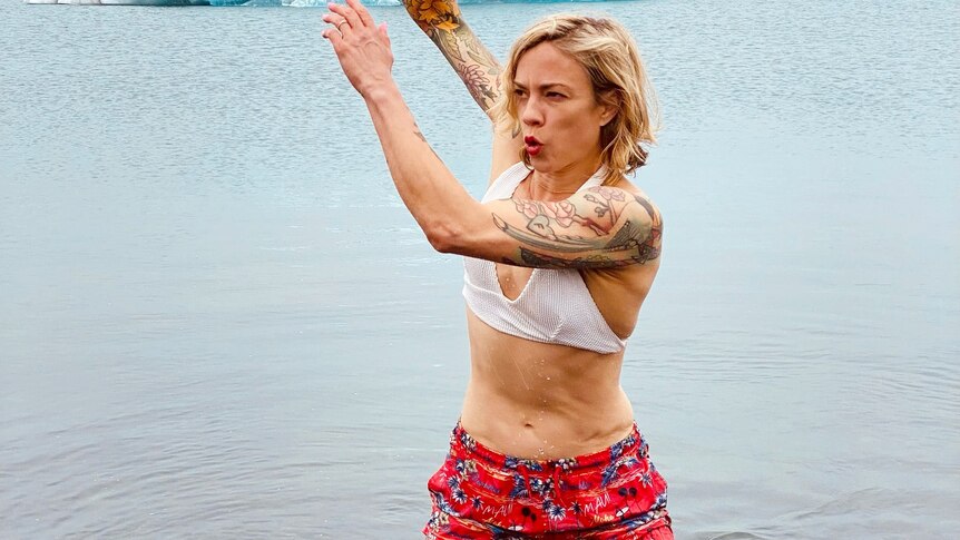 Jenny Valentish, in white crop top and short red shorts, has shocked expression and arms raised, surrounded by clear water.