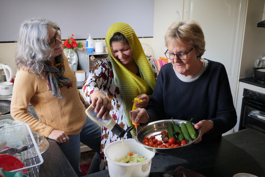 Three women prepare vegetables for a meal in a kitchen