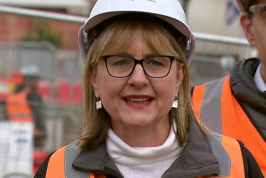 a blonde woman wearing glasses, a hard hat and a high-vis vest. 