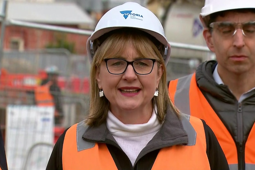 a blonde woman wearing glasses, a hard hat and a high-vis vest. 