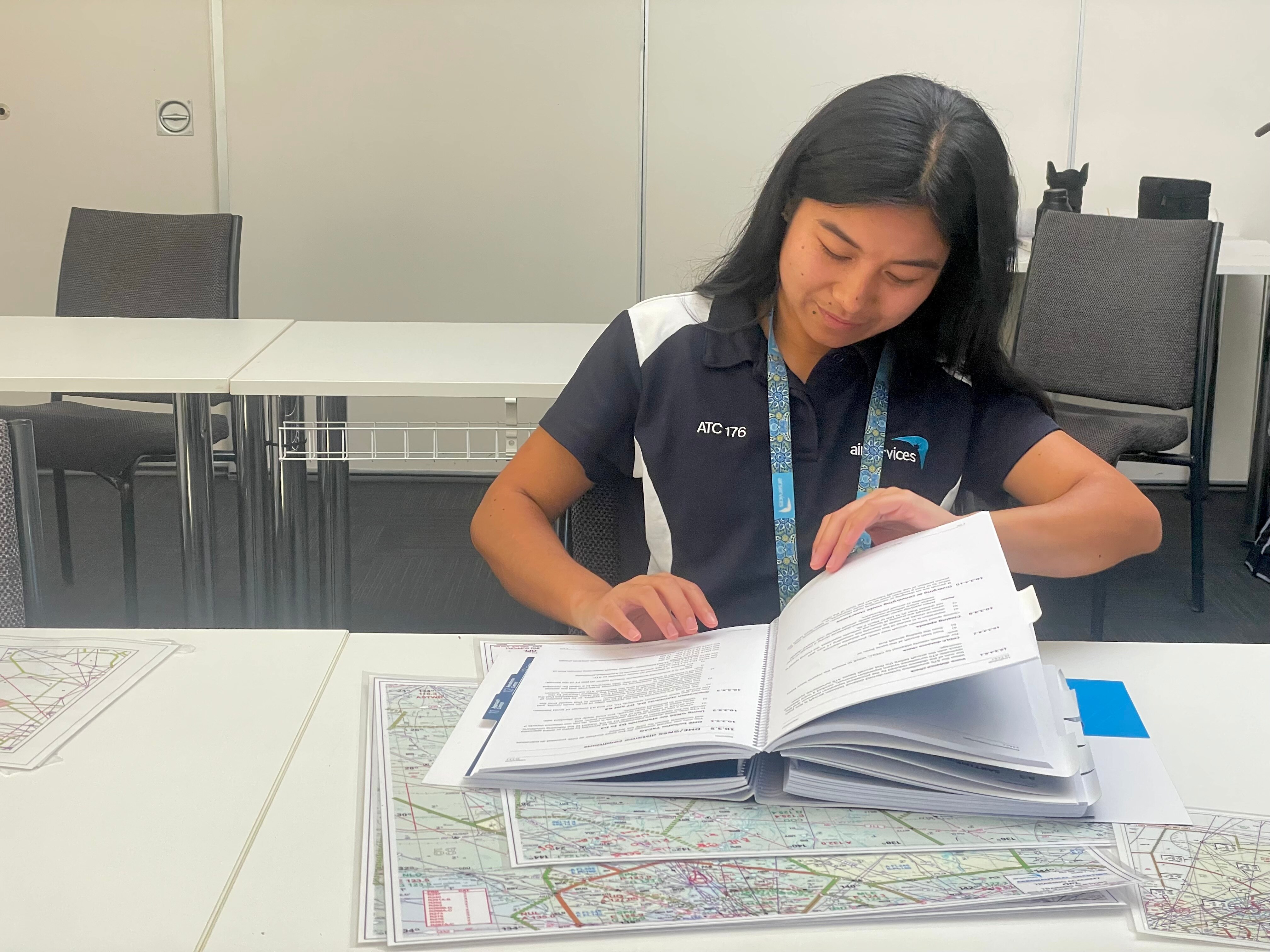 Young woman in a blue shirt reading a textbook at a desk.