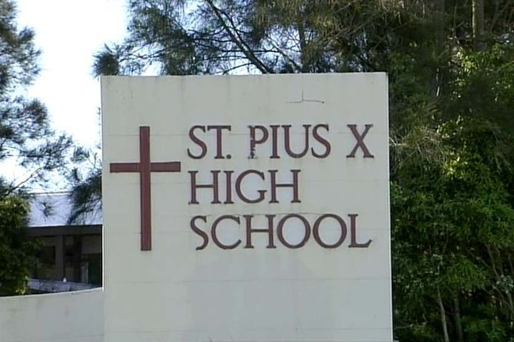 A photo of a school sign that says 'St Pius X High School' alongside a Christian cross.