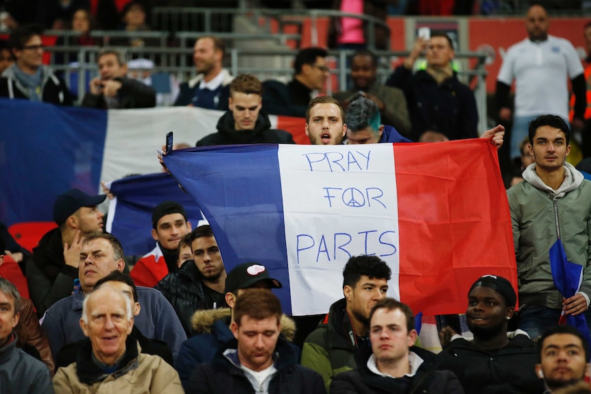 A man holds a French flag emblazoned with "Pray for Paris"