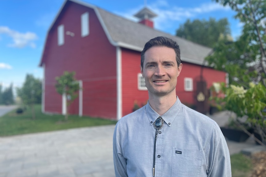 A man stands in front of a red barn