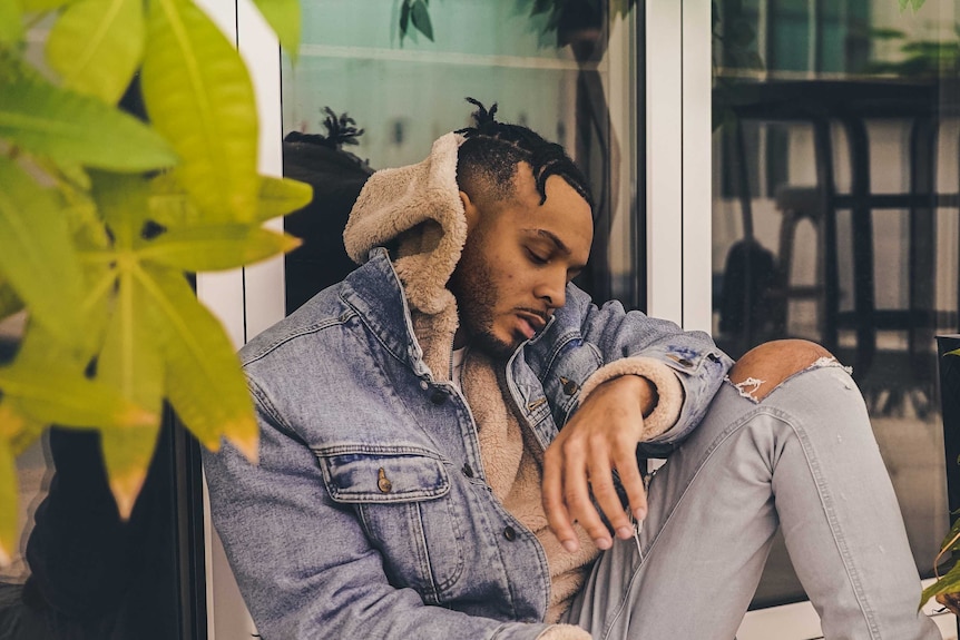 Man sits along bench in denim jacket and jeans to depict theories about denim, such as buying jeans too tight.