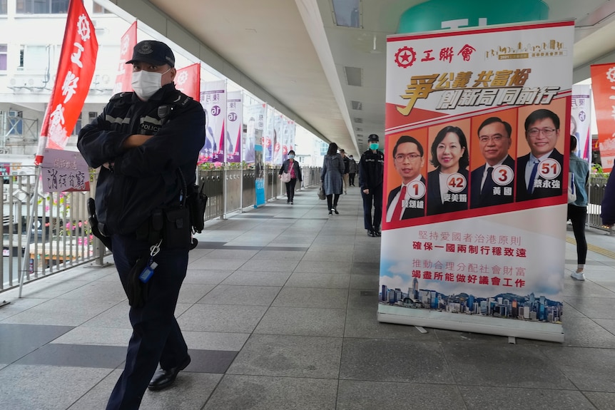 A Hong Kong police officer walks past a poster of pro-Beijing candidates
