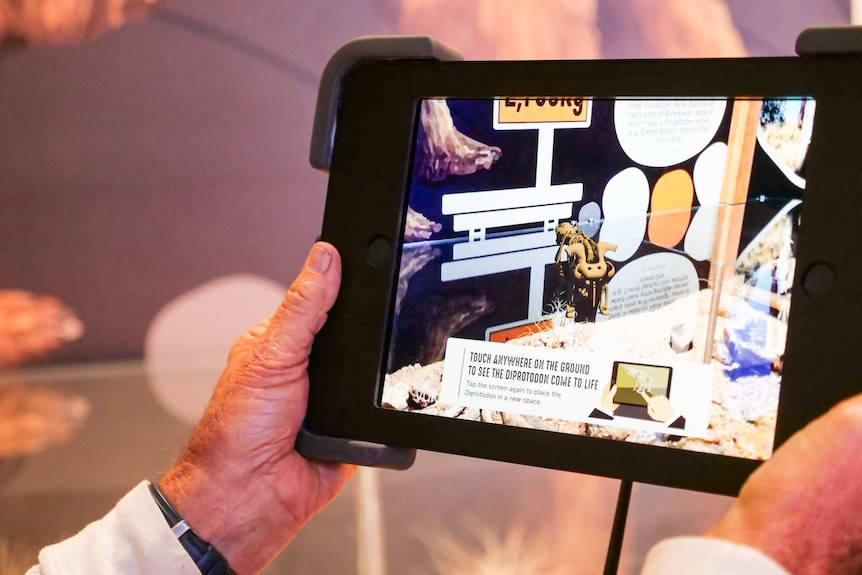Hands hold an iPad which showcases an augmented reality fossil experience.