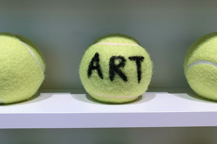 A yellow tennis ball with the word ART written on it with black marker