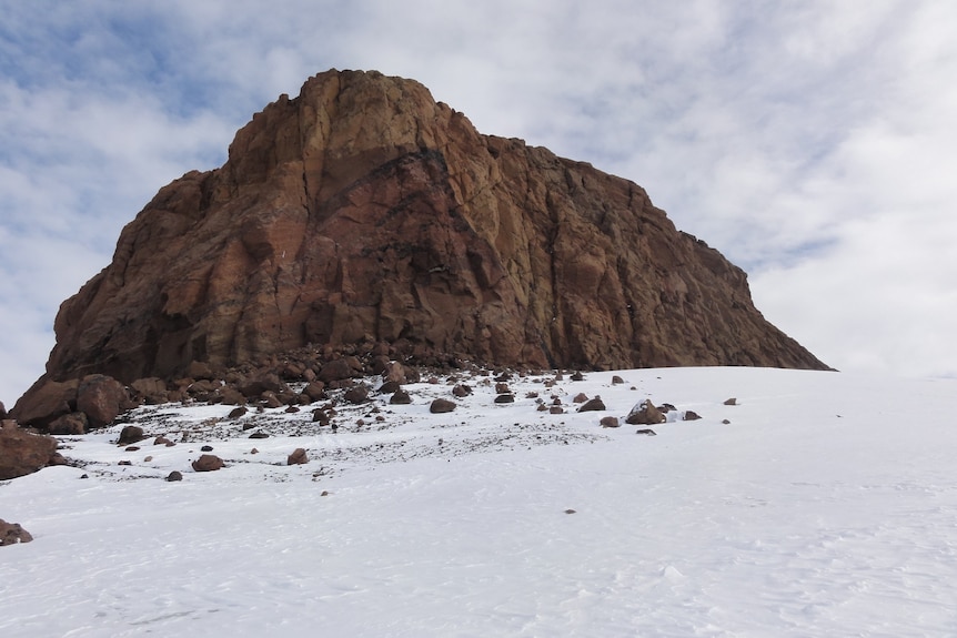 A large rocky cliff face, with a snowy slope leading up to it.