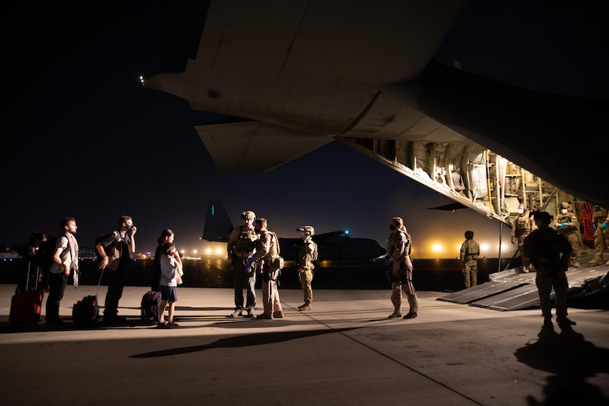 A number of ADF troops standing at the back of a large aircraft with its ramp down, lit up by the light inside the plane