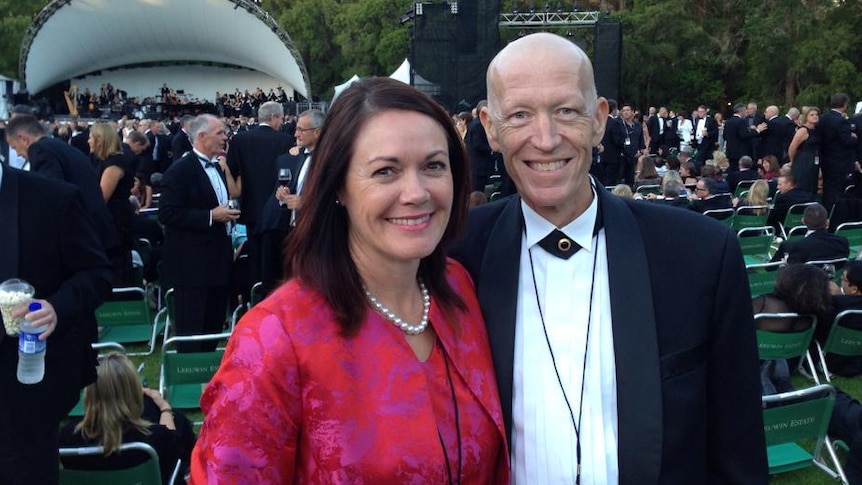 A smiling woman in a red blouse with a man in a jacket at an outdoor concert