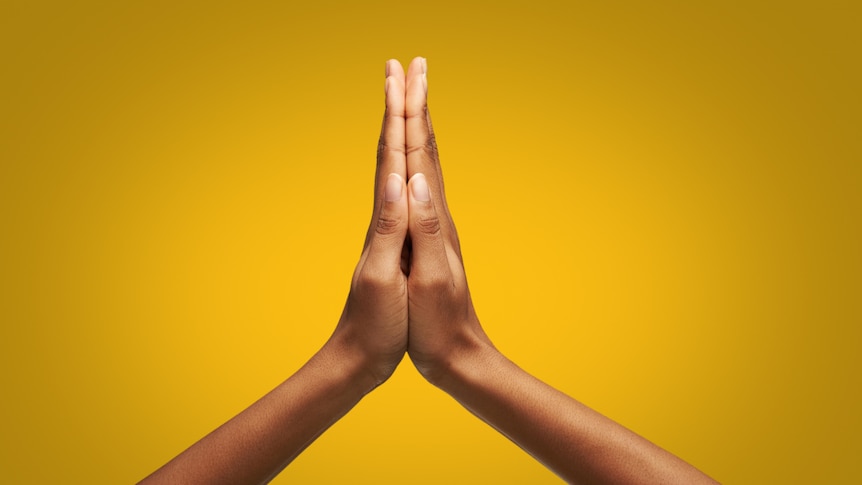 two hands clasped together in prayer motion against yellow background