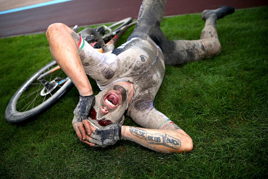 Covered in mud, Sonny Colbrelli lies on his back next to his bike, holds his hands to his head and screams