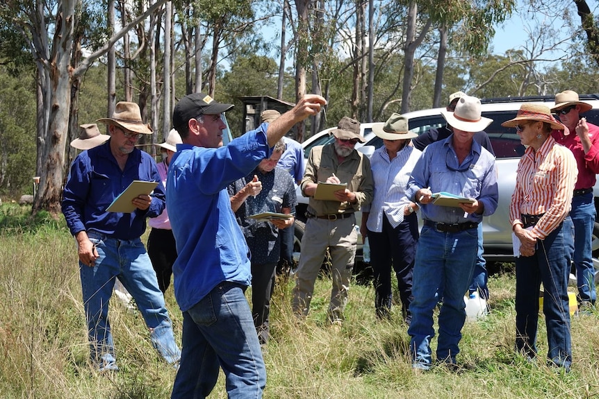 A man talking to a group in a paddock.