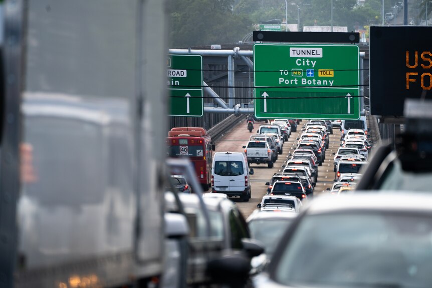 La imagen muestra congestión y retrasos en el tráfico.  Puedes ver autos, camino gris en un día sombrío.