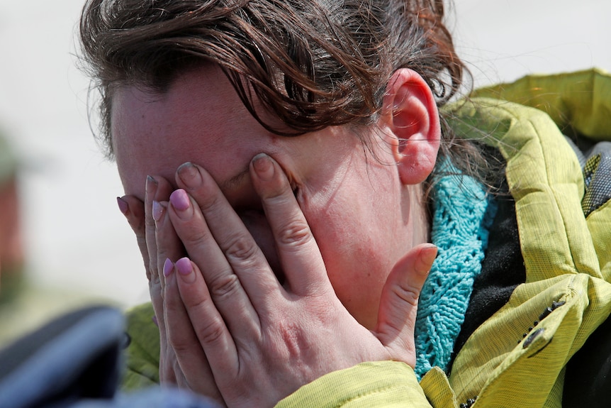 A woman covers her face with her hands as she cries.
