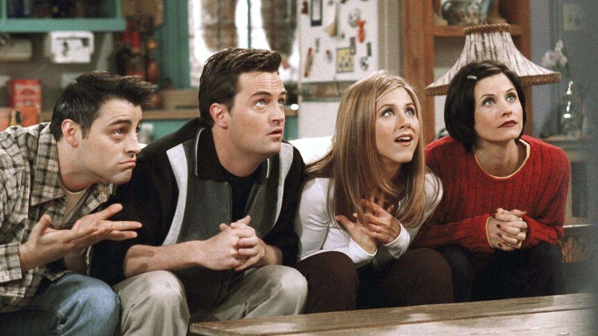 A still from the TV show Friends, showing characters Joey, Chandler, Rachel and Monica on a couch, all looking up expectantly.