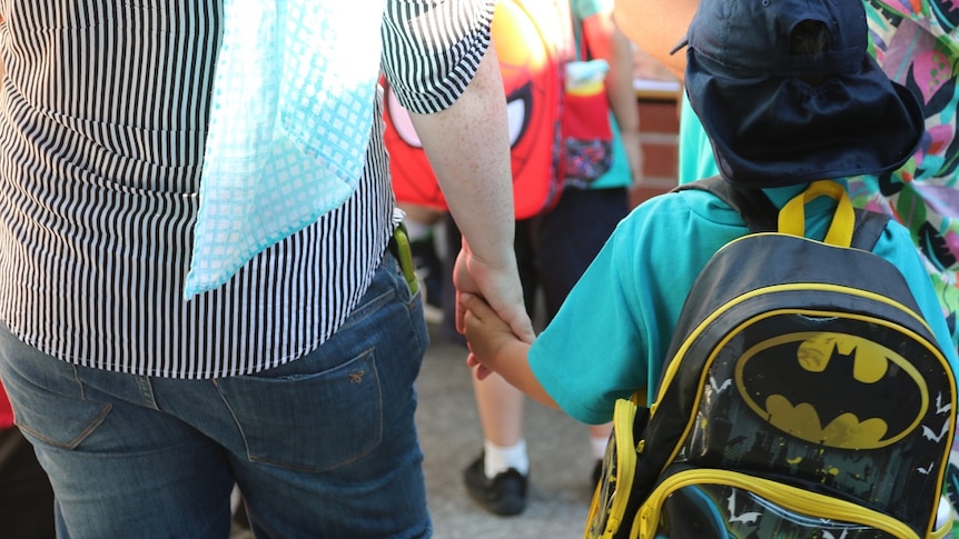 Young boy holds his parent's hand as he waits in line for his first day of kindergarten.