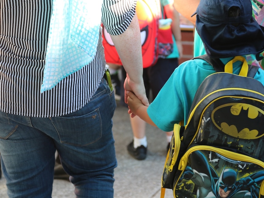 Young boy holds his parent's hand as he waits in line for his first day of kindergarten.