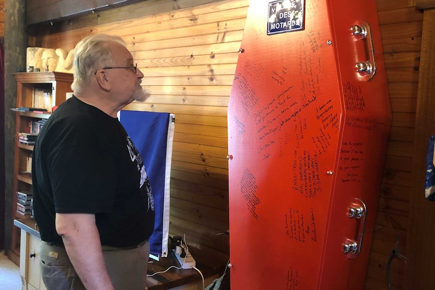 Bertand Cadart stands in his loungeroom looking at a red coffin with writing on it.