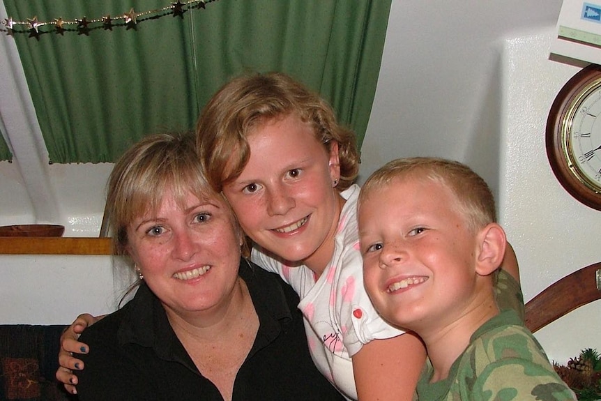 A woman gets hugged by two children sitting down