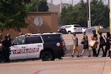 People are pictured walking towards a police car with their hands up.