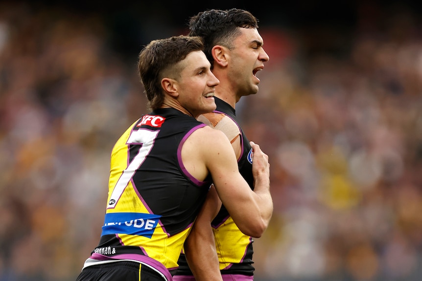 Two Richmond AFL players embrace as they celebrate a goal.