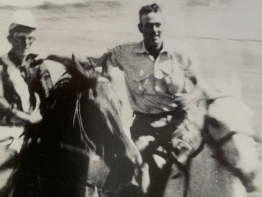 A black and white photo of two men on horseback.