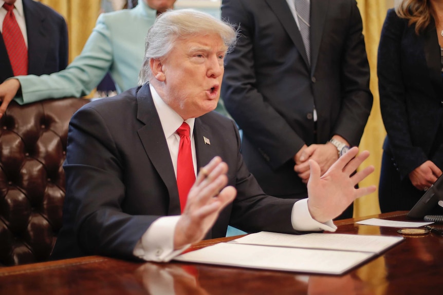Donald Trump gestures at the signing of his 'one in, two out' executive order