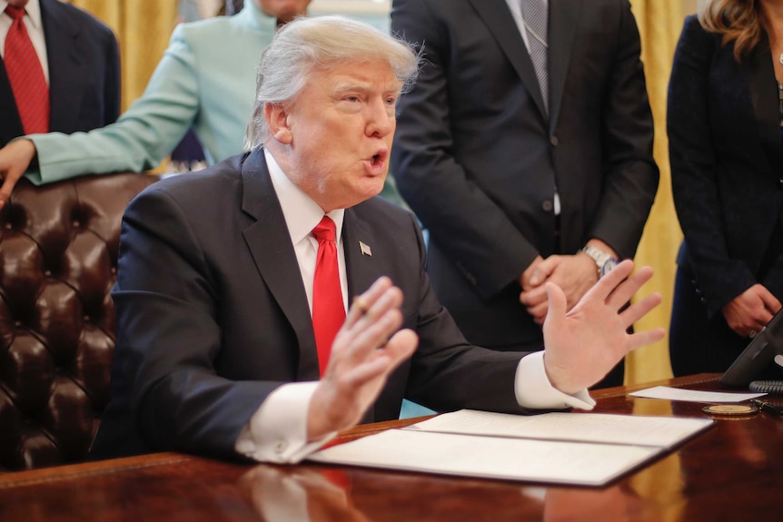 President Donald Trump gestures with both hands and furrows his brow as he speaks in the Oval Office.