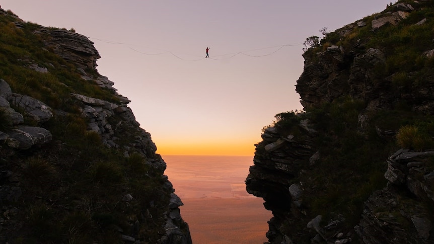 A walker on a tightrope between two rocky outcrops at sunrsie