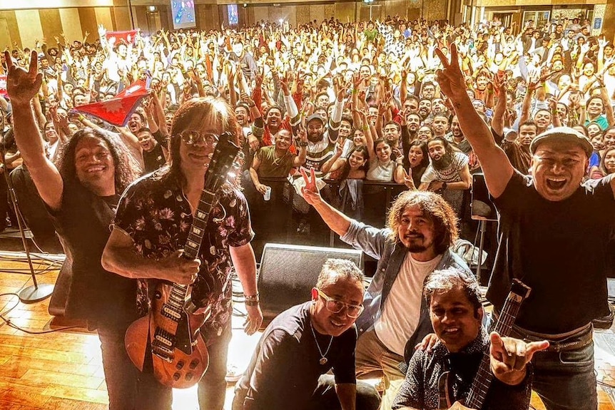 Six Nepalese men on a stage in front of a crowd.