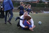 Morrison in a tie tackles a small child, with a soccer ball behind him